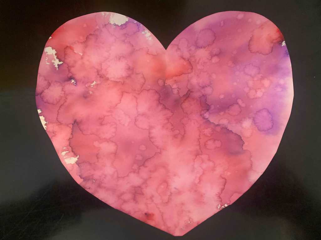 A cut out heart on a black background. The heart has blended red, pink, and purple colors in it, along with the shapes of water rivulets and droplets.