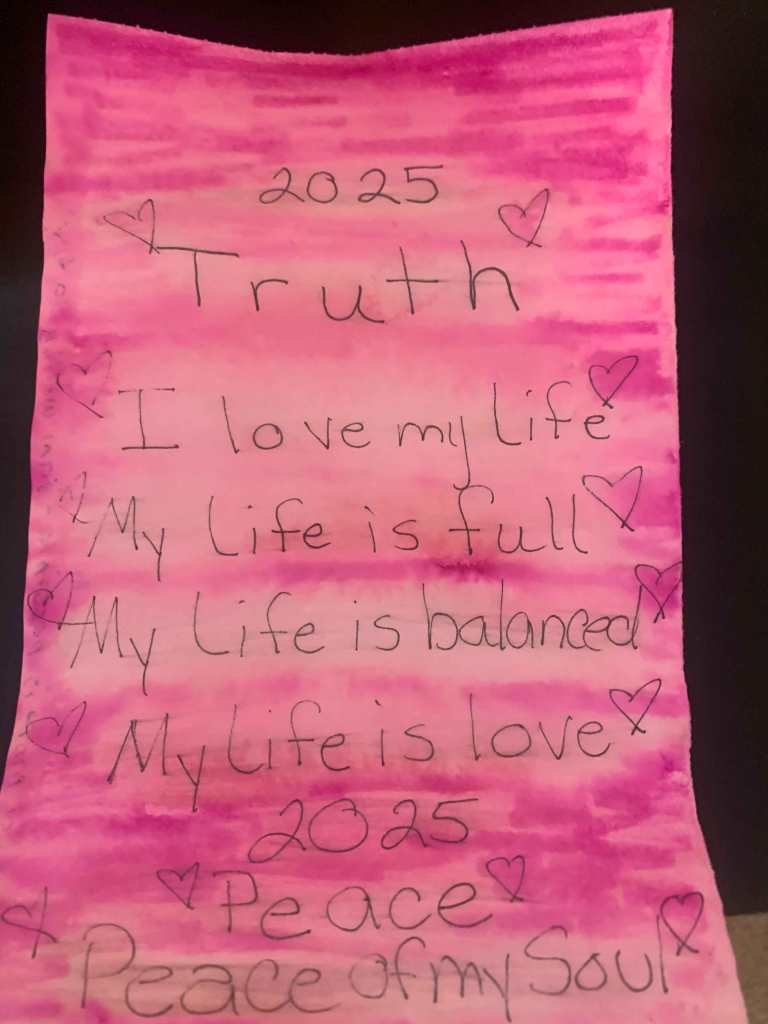 A page of blended shades of pink with an affirmation on it. There are small hand drawn hearts around the affirmation. The writing on it reads: 2025. Truth. I love my life. My life is full. My Life is balanced. My life is Love. 2025. Peace. Peace of my Soul.